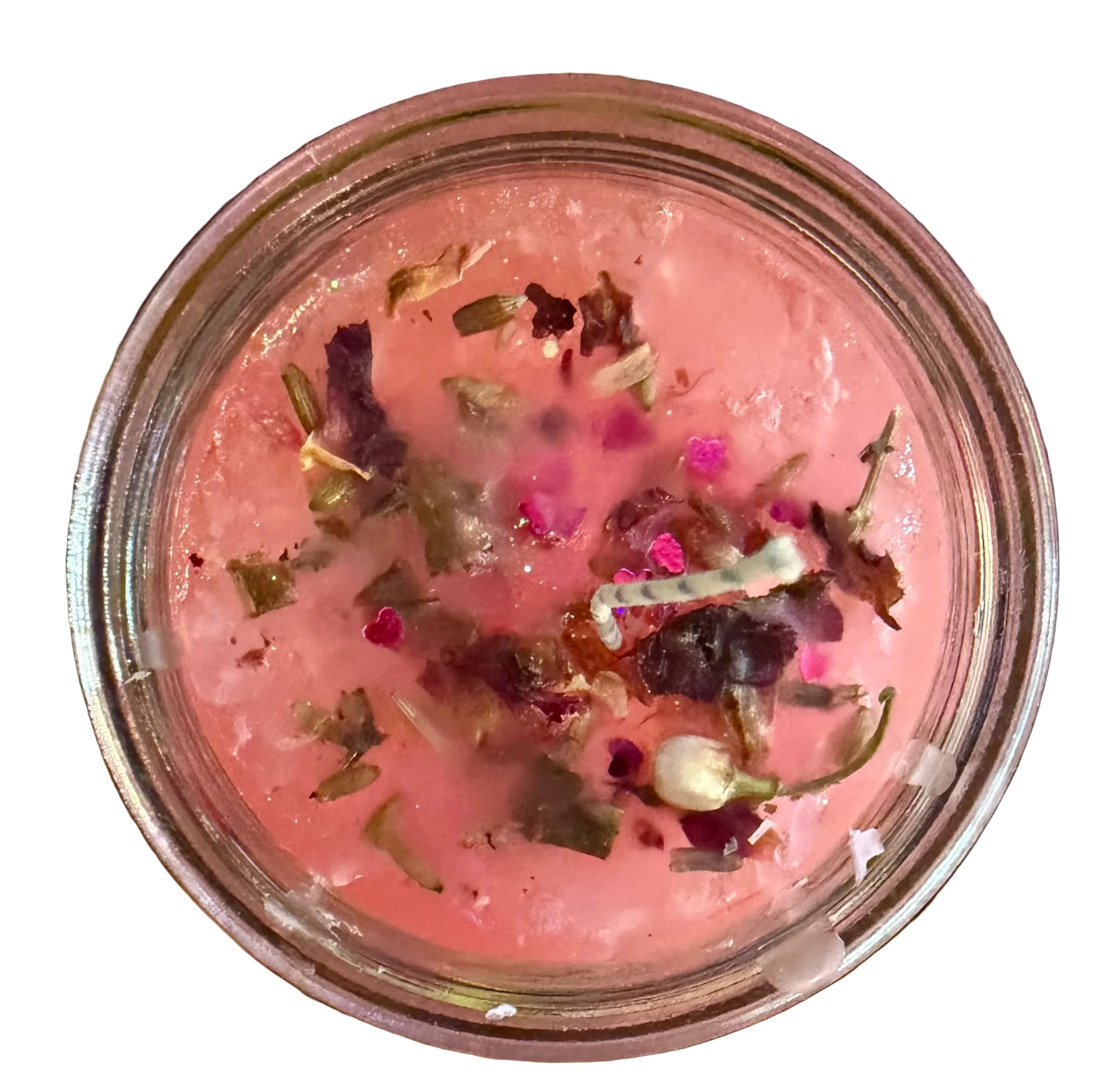 A close-up top-down view of a pink candle in clear glass, containing dried flower petals, and small pink and green botanical pieces.