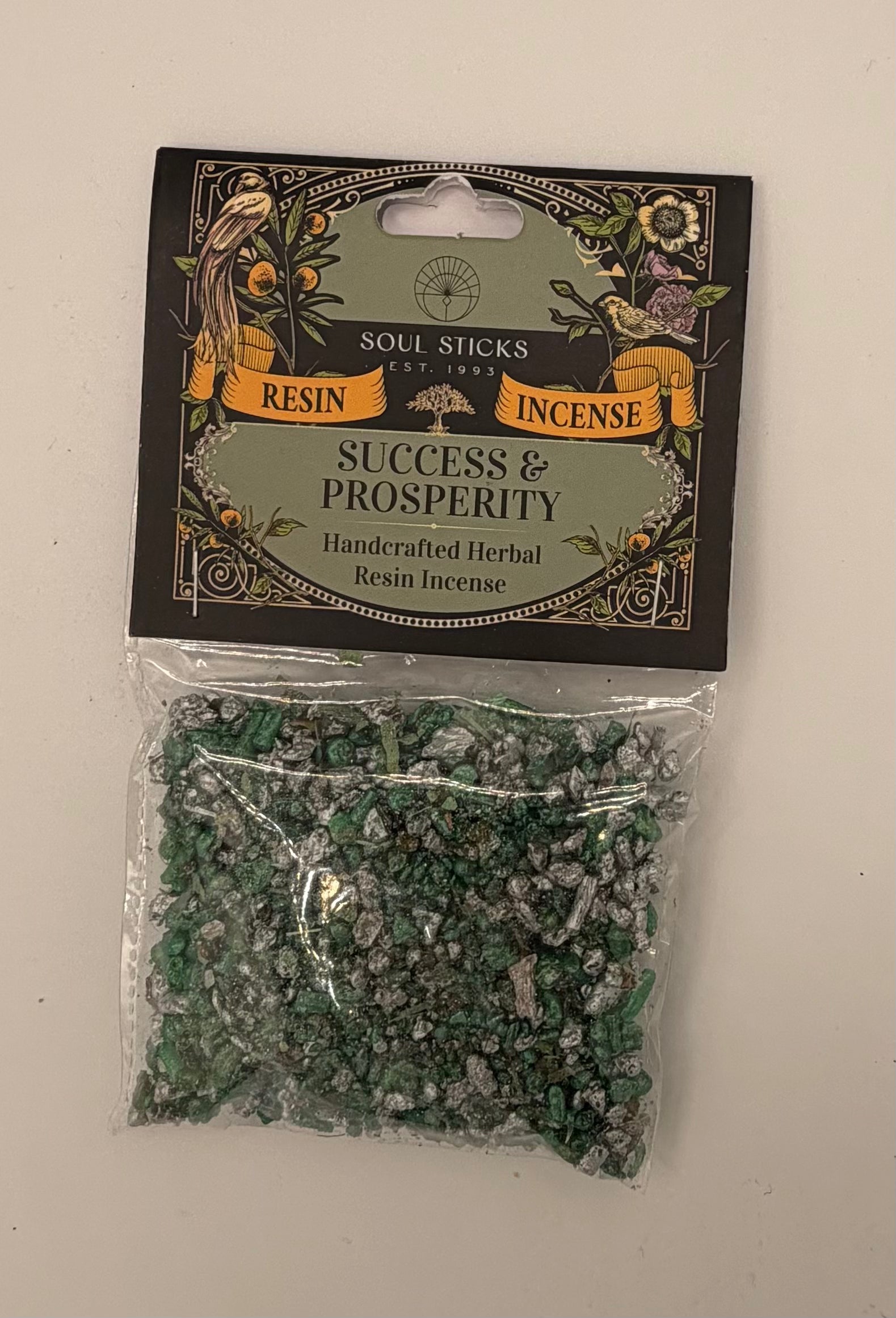 A package of Soul Sticks Incense, specifically 'Success & Prosperity' handcrafted herbal resin incense. The product consists of green and silver resin chips inside a clear plastic bag, sealed with a decorative black header card featuring gold and green illustrations.