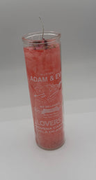 A pink devotional candle in a clear glass jar with a wick, featuring white printed text and heart designs on a neutral gray background.